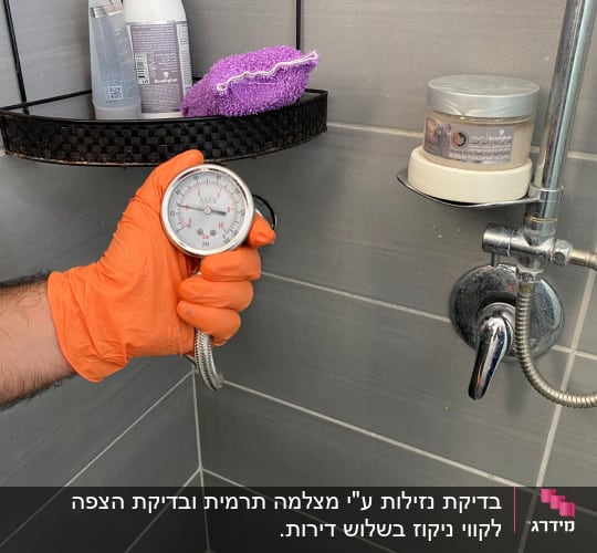 מד לחץ מים מוחזק ביד עם כפפה כתומה במקלחת